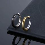 Detail view of matte titanium steel hoop earrings in black and gold on a reflective surface