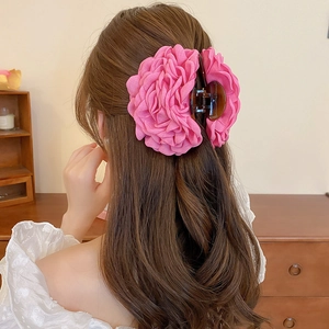 Detail of large pink fabric flower hair claw clip on model's hair in home setting