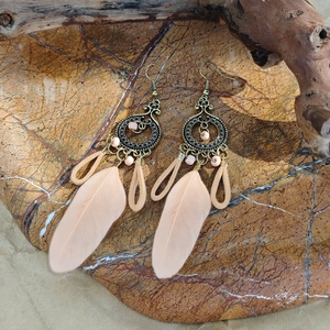 Macro detail of Bohemian feather earrings with pink beads on a rustic stone background