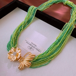 Détail du collier de perles vertes avec fermoirs papillon et fleur dorés en strass