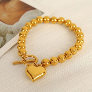 Elegant gold beaded bracelet featuring a heart pendant and toggle clasp on beige fabric