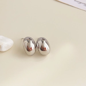 Macro detail of polished silver oval stud earrings on a minimalist decorative desk setup