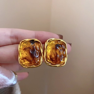 Detail of square amber resin earring with gold twisted metal frame texture