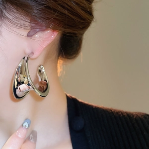 Close-up of a silver-tone twisted C-shape metal earring on a model with glossy finish