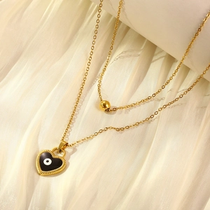 Detail of double-layer gold chain with heart-shaped evil eye pendant on soft beige fabric