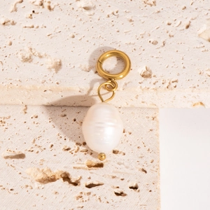 Detail of baroque pearl pendant with gold metal ring on beige travertine stone display