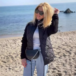 Detail of a black quilted jacket with knit sleeves and stand collar on a beach setting