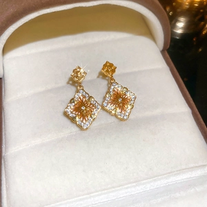 Détail de la boucle d'oreille fleur plaquée or avec zircons sur un écrin en velours doux