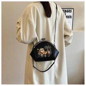 Detail shot of a black shell bag with floral embroidery and chain strap on a beige coat
