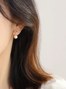 Detail of elegant gold knot earring with white pearl drop on a model