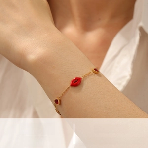 Detail of gold chain bracelet with red lips charm and heart-shaped red zircon stones