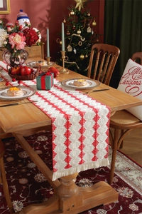 Detail of red and white woven Christmas table runner with white tassels on a wooden table