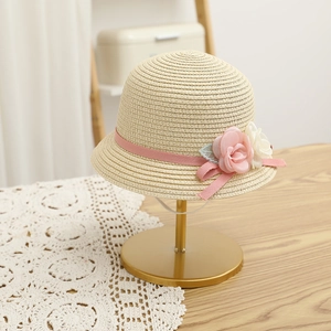 Detail of beige straw hat featuring woven pink ribbon, floral accents and lace leaves