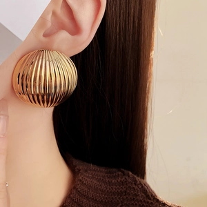 Close-up of gold round textured earrings with vertical stripes on a female model