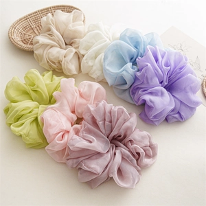 Detail of seven large solid chiffon hair scrunchies in pastel colors on a beige background