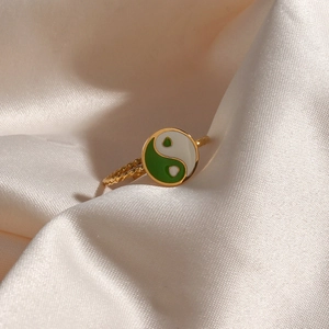 Macro shot of 18K gold plated ring with green and white yin yang design on beige silk