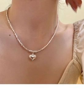 Detail of silver heart pendant necklace with pearl beads worn by a model on collarbone