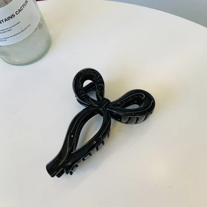 Glossy black ribbon bow claw clip with hair teeth on a clean white surface detail