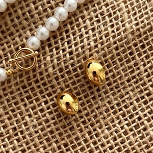 Close-up of golden oval stud earrings and a white pearl necklace with OT toggle clasp