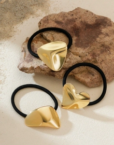 Three gold heart-shaped metal hair ties on beach sand, high elasticity black elastics
