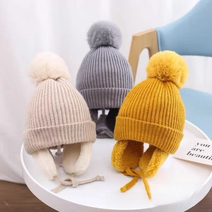 Detail of warm knit baby hats in cream, grey and yellow with pom-poms and fleece lining
