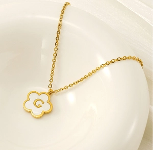 Close-up of gold clover necklace with white shell pendant and engraved letter G detail