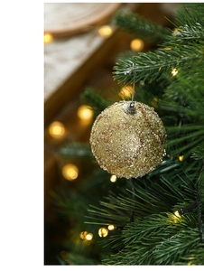 Close-up of golden Christmas ball with sequins hanging on a green festive tree branch
