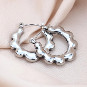 Macro shot of silver wavy hoop earrings on beige satin with polished mirror finish