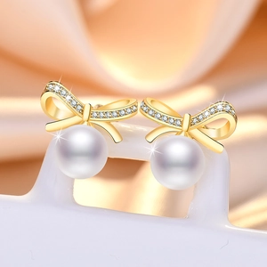 Sparkling zircon bow earrings with round white pearl drop on warm silk background