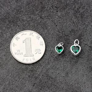 Macro view of heart-shaped emerald green zircon pendant in S925 silver with coin for scale