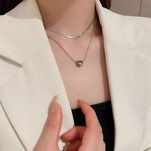 Close-up of double-layer silver heart necklace and snake chain on model in white suit