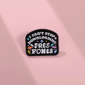 Macro detail of black enamel brooch featuring stylish typography on a pink background