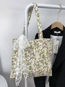 Detailed close-up of a floral canvas tote bag featuring a large white lace bow accent