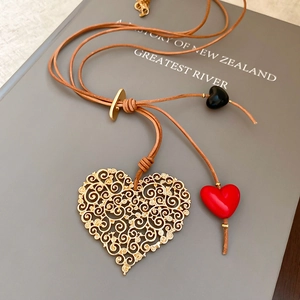 Detail of a large hollow gold heart pendant with red and black heart beads on a leather cord