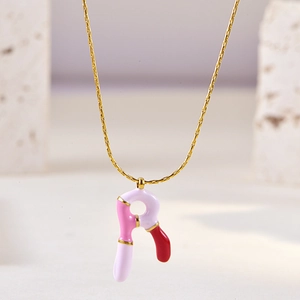 Detail of pink and white enamel letter pendant on a gold necklace with stone background