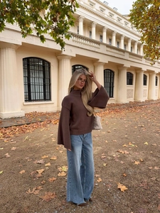 Dettaglio di un maglione oversize a collo alto marrone scuro abbinato a jeans larghi in autunno