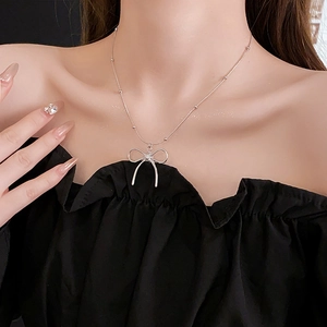 Detail of a silver bow pendant necklace on a model showing the elegant titanium steel chain