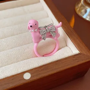 Pink enamel puppy ring with pearl collar and rhinestone bow on cream fabric display