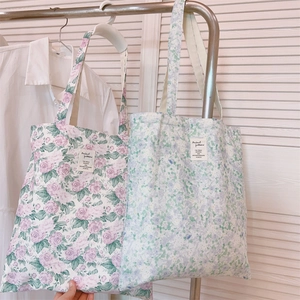 Detail of floral canvas tote bags in pink rose and green patterns hanging on a rack