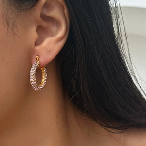 Close-up of gold geometric hoop earrings with clear pavé zircon stones on model