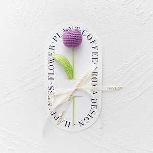 Detailed close-up of handmade purple knitted tulip with green leaves and silk ribbon