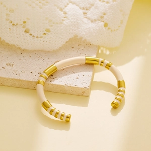 Detail of gold and off-white enamel segmented bangle placed on textured travertine stone