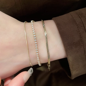 Detailed close-up of a gold snake chain and zircon tennis bracelet set on a model wrist