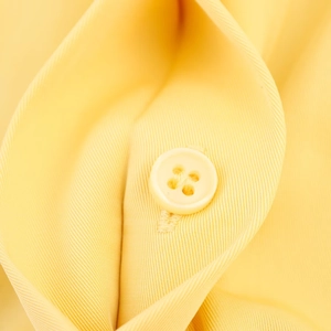 Detailed macro view of yellow twill fabric and beige four-hole resin buttons on a dress
