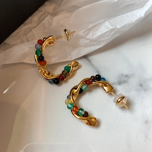 Ethnic C-shaped stone beaded earrings in gold finish on white marble texture surface