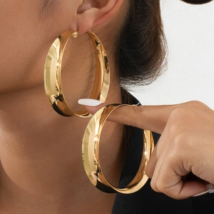 Close-up of model wearing large gold hoop earrings with bright metallic luster