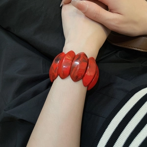Detailed close-up of a red marble acrylic oval bracelet worn on a wrist in a fashion setting