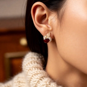 Detail of 18k gold plated earring with deep red pearl and shimmering zircon bow design