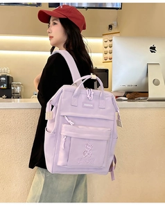 Side view of a purple nylon backpack with bear embroidery in a cozy cafe setting