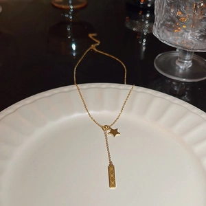 Detailed close-up of a gold star and geometric bar pendant necklace on a ceramic plate